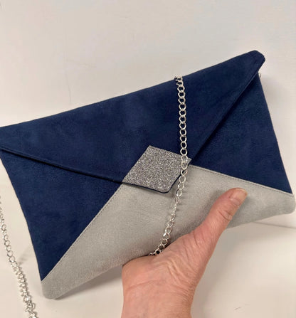 Le sac pochette Isa bleu marine et gris à paillettes argentées, avec sa chainette amovible, porté à la main.