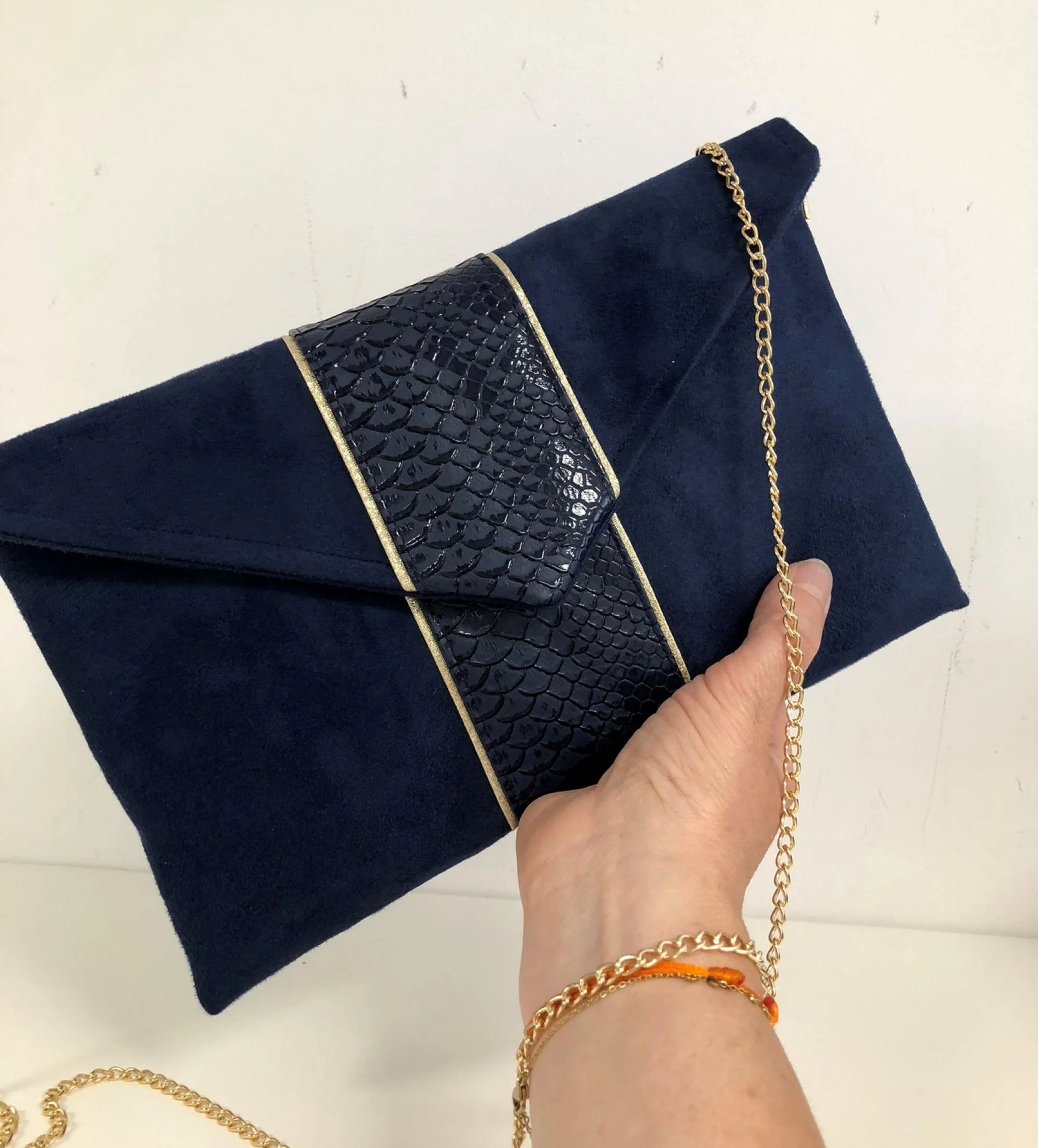 Le sac pochette Isa bleu marine reptile à liseré doré, porté en main.