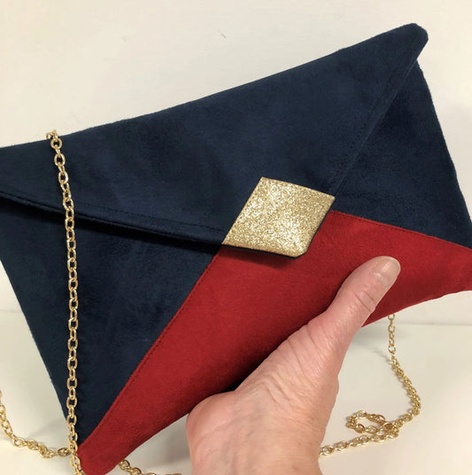 Le sac pochette Isa bleu marine et rouge à pailettes dorées, tenu en main.