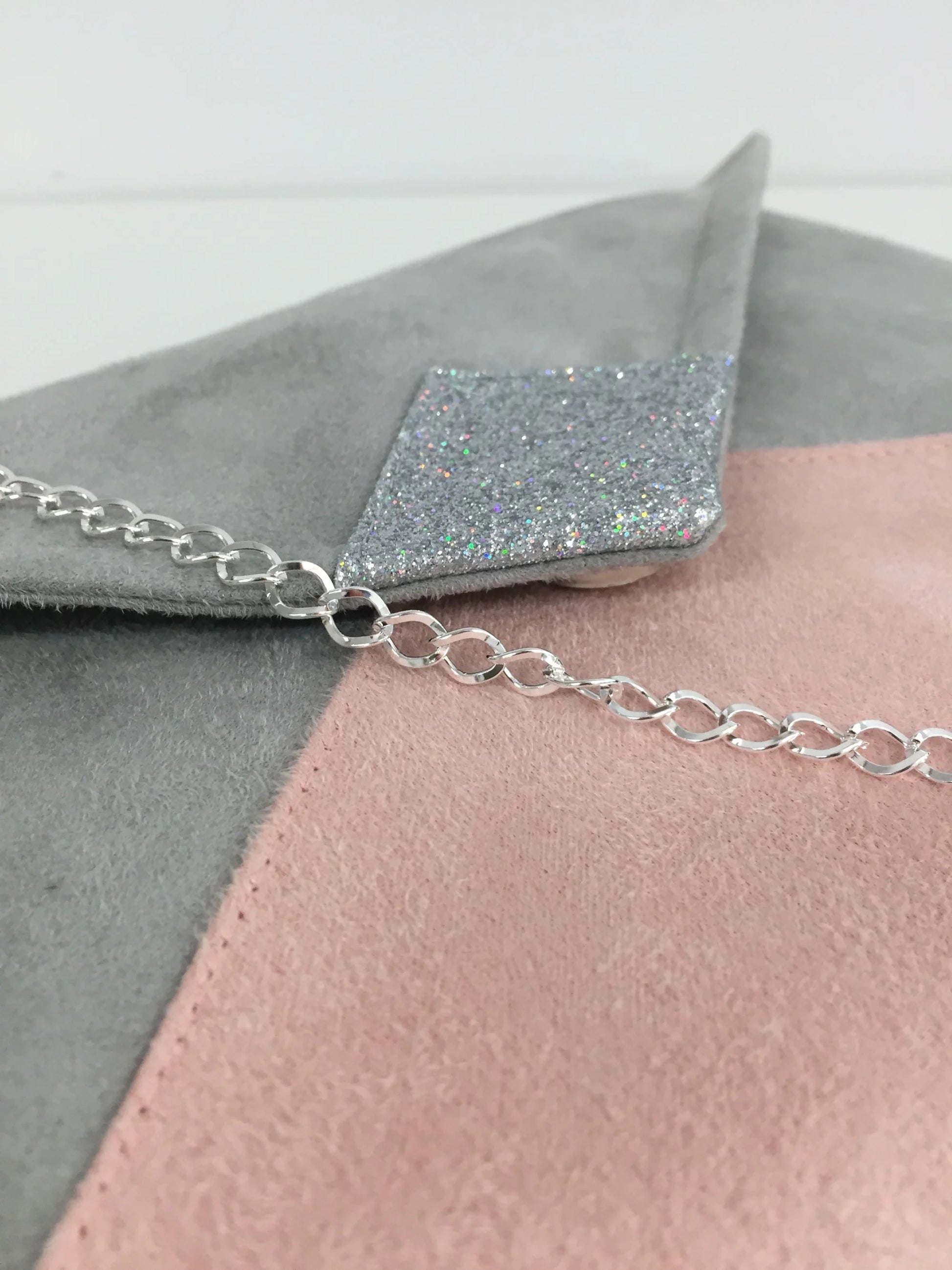 Vue détaillée du sac pochette Isa gris clair et rose poudré à paillettes argentées, avec sa chainette amovible.