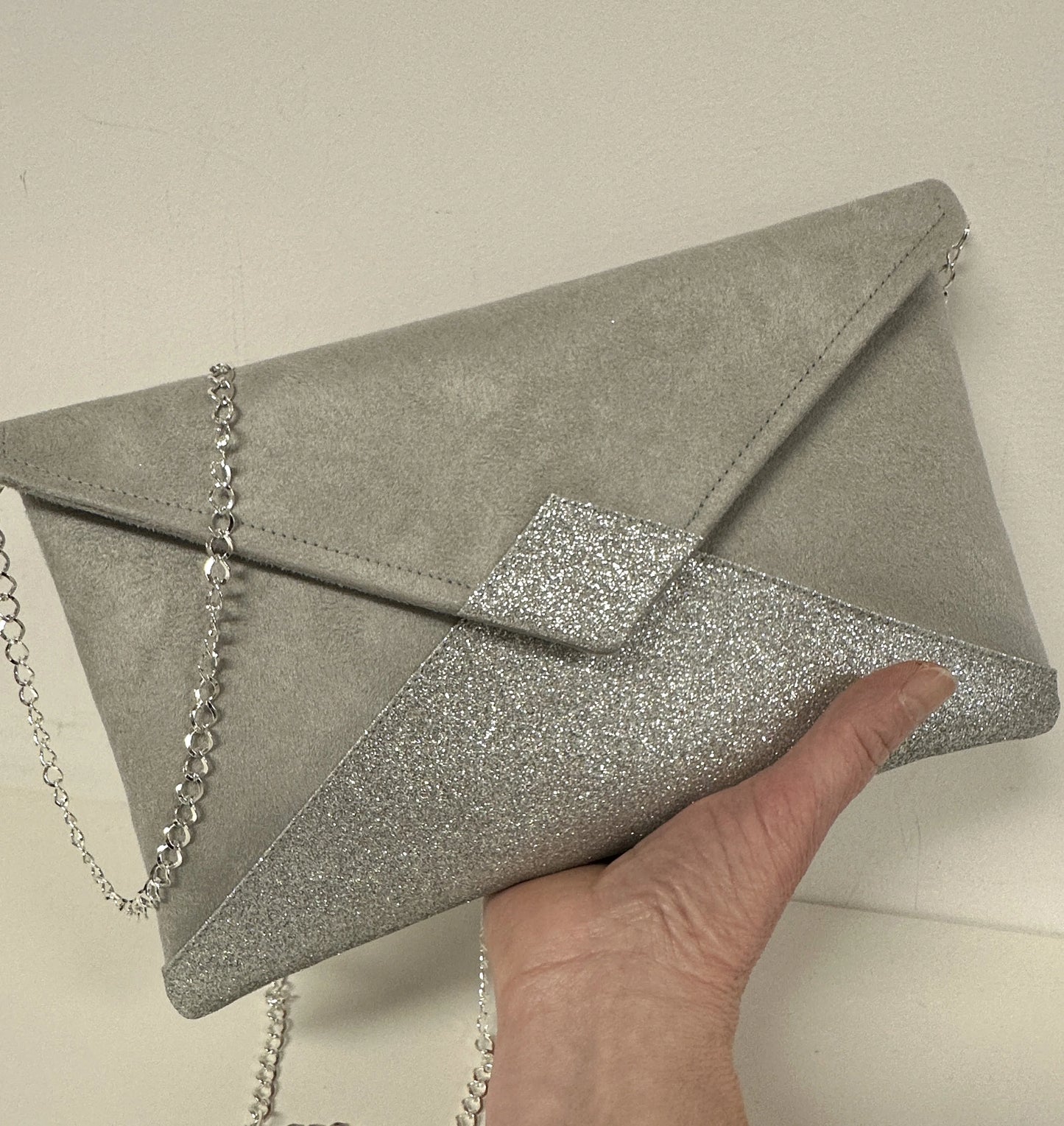 Le sac pochette Isa gris perle à paillettes argentées, avec sa chainette amovible.