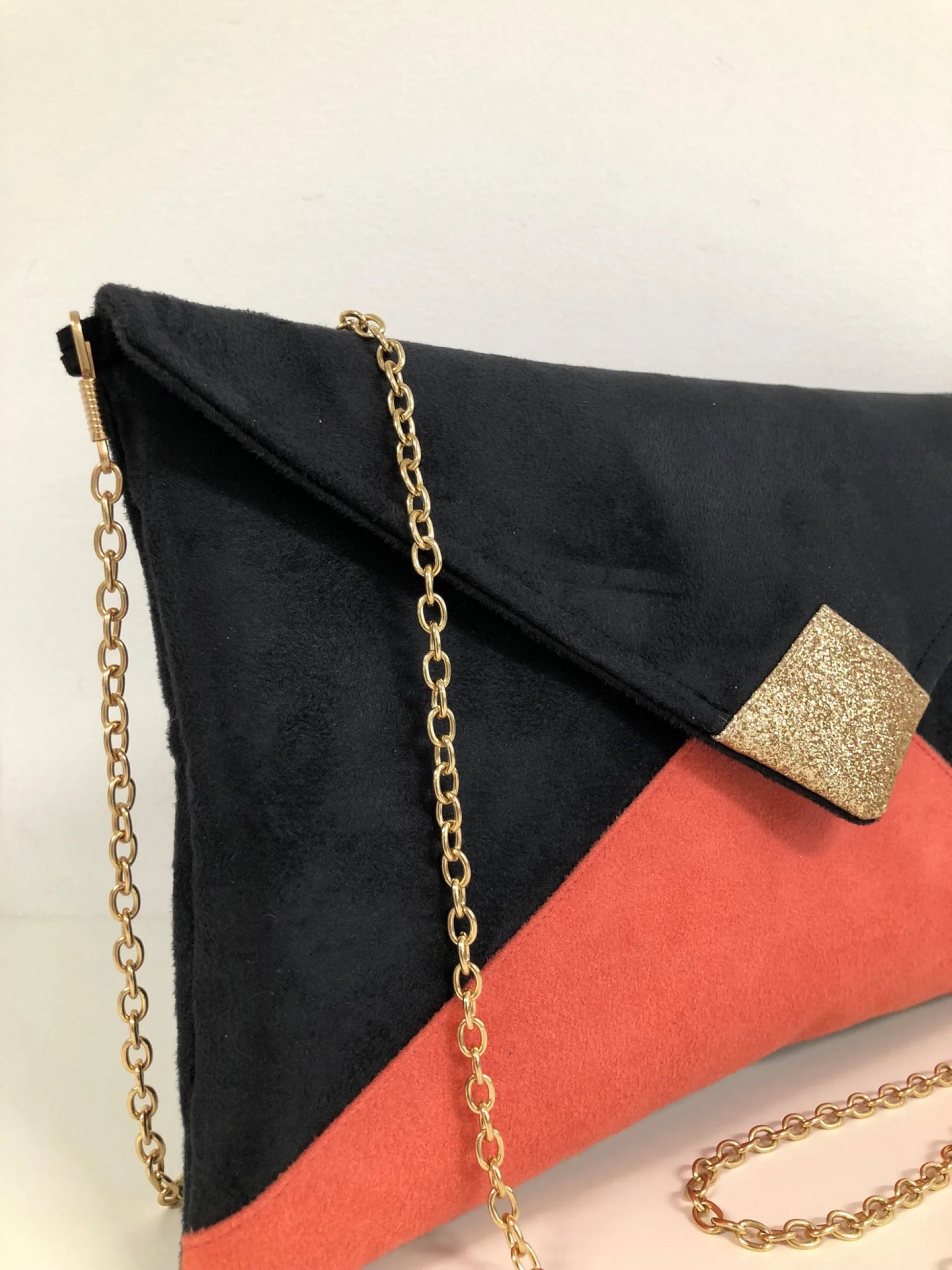 La chainette dorée amovible du sac pochette Isa noir et corail à paillettes dorées.