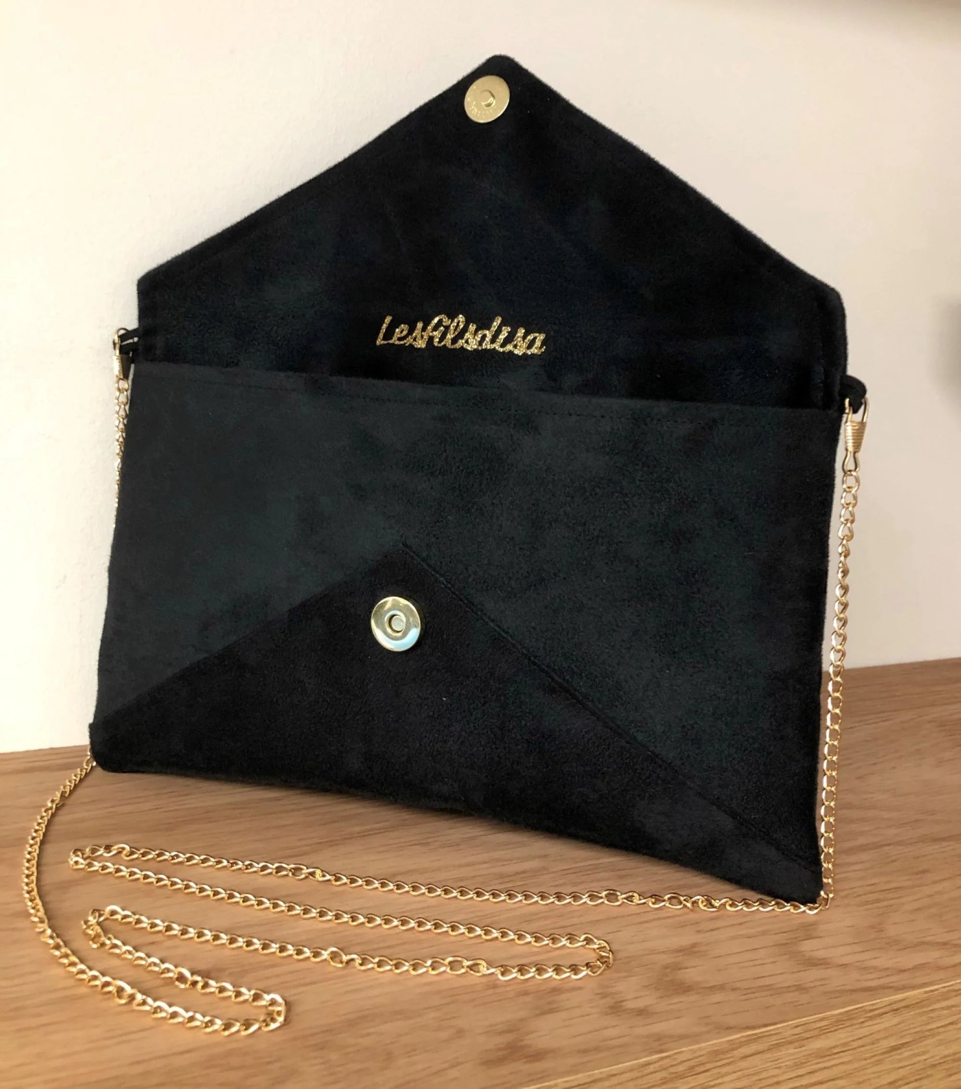 Le sac pochette Isa en suédine noire et paillettes dorées, ouvert,  avec chainette amovible.